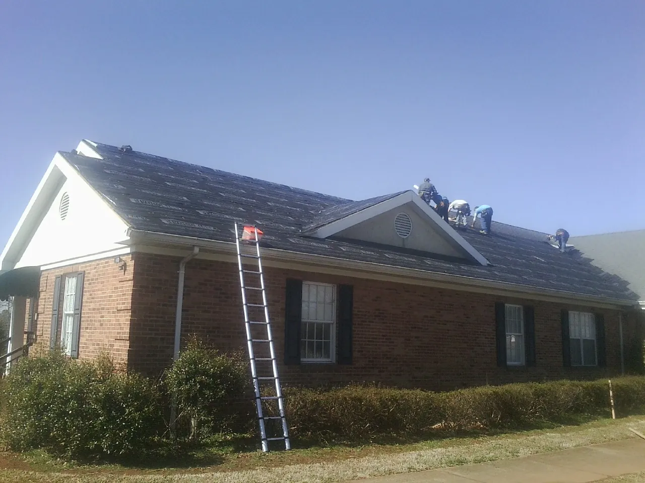 Crew tearing shingles off a brick ranch roof with a ladder set — Emergency Roof Repair work by our crew in Frankton