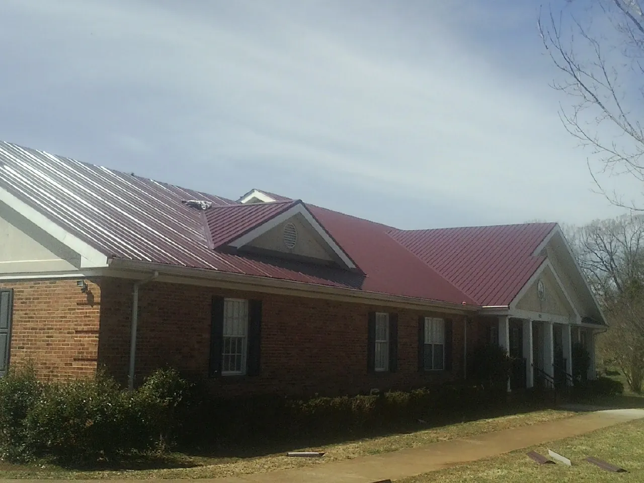 Red metal roof with gabled entries on a long brick building, from a Hail Damage Roof Repair job in Frankton