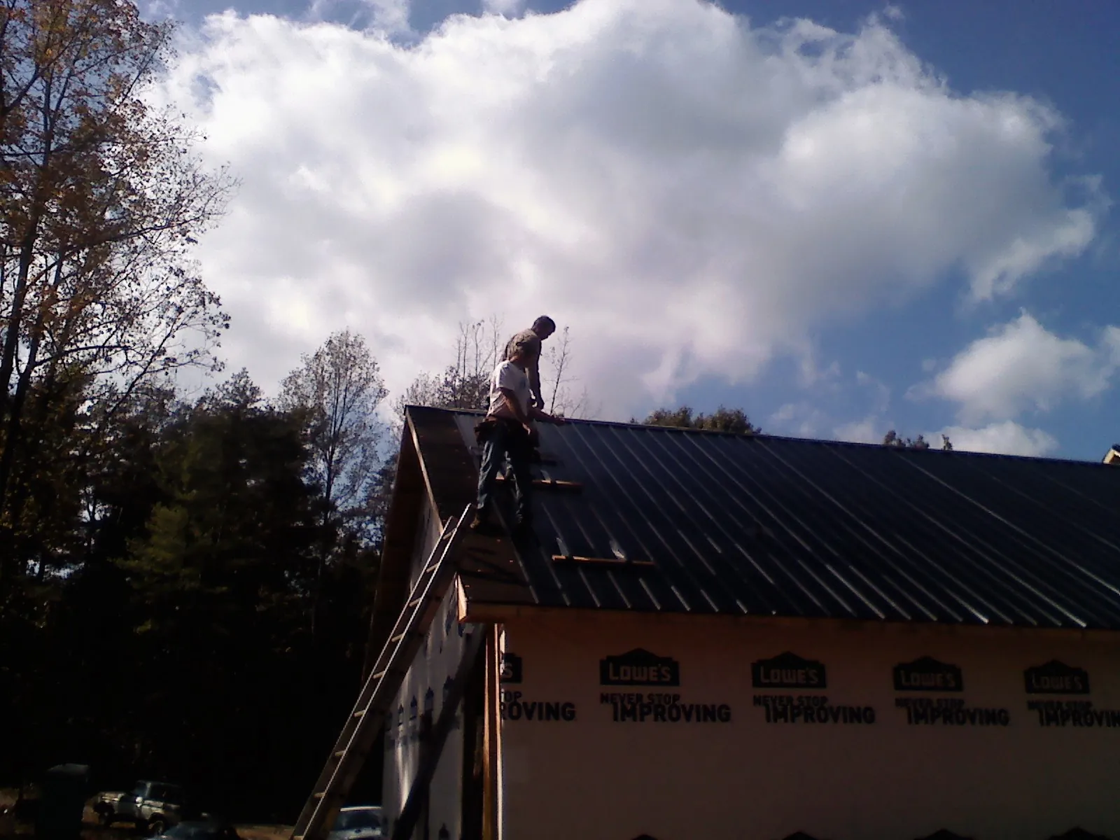Roofer fastening dark metal panels high against a cloudy sky, from a Roof Inspection job in Frankton