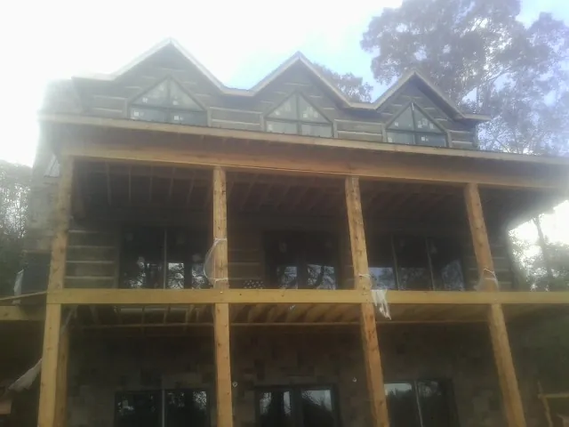 Dormers and porch framing on a large log home under construction — Roof Coating work by our crew in Frankton