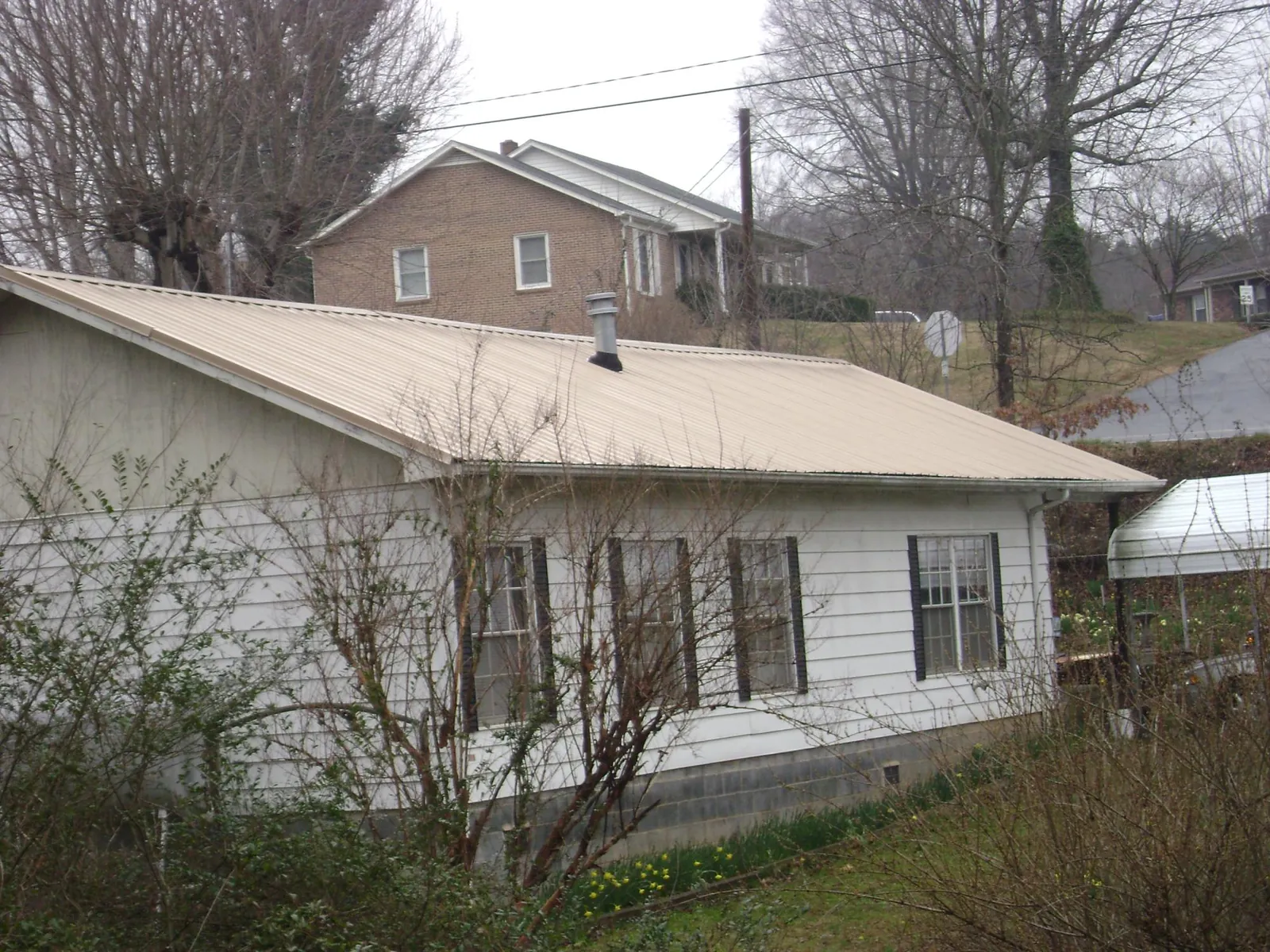 Tan metal roof on a white sided house set into a hillside — Commercial Roofing by Roofing Brothers in Frankton