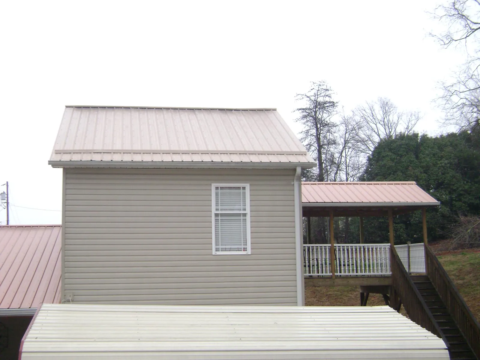 Tan metal roofs on a two story addition and attached porch, from a Roof Replacement job in Frankton